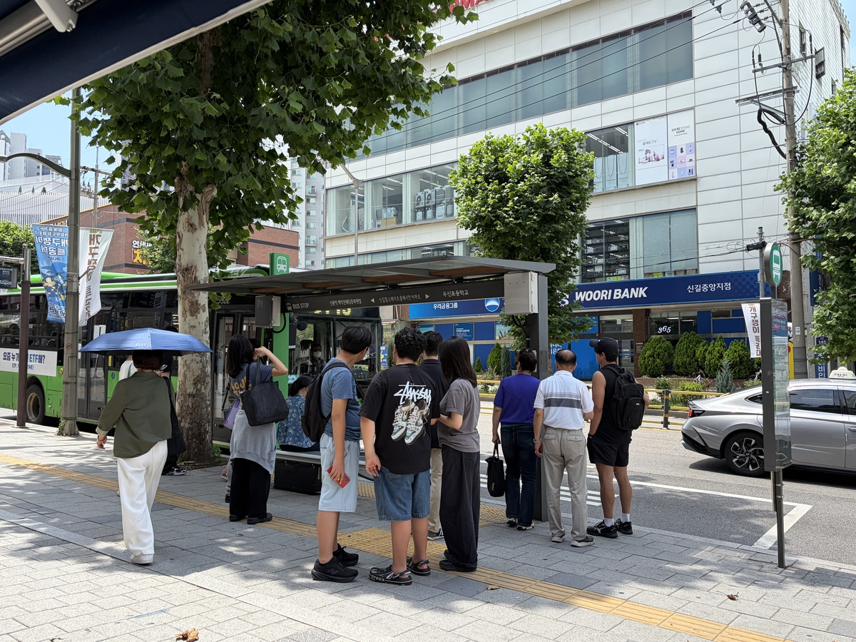 나무 그늘에 모여 버스 기다리는 시민들